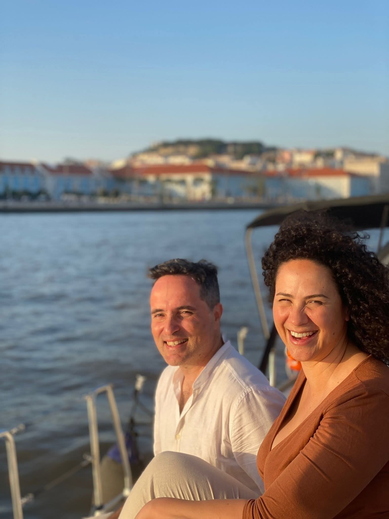 Paulo Alexandrino e Yara Nunez, fundadores da Lusitana Boat, a bordo no rio Tejo com Lisboa ao fundo